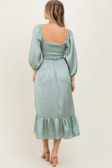 woman wearing a sage green backless midi dress with puff sleeves and ruffled hem