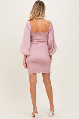woman wearing a light pink maternity dress with smocked detailing and balloon sleeves, showing her baby bump from the back