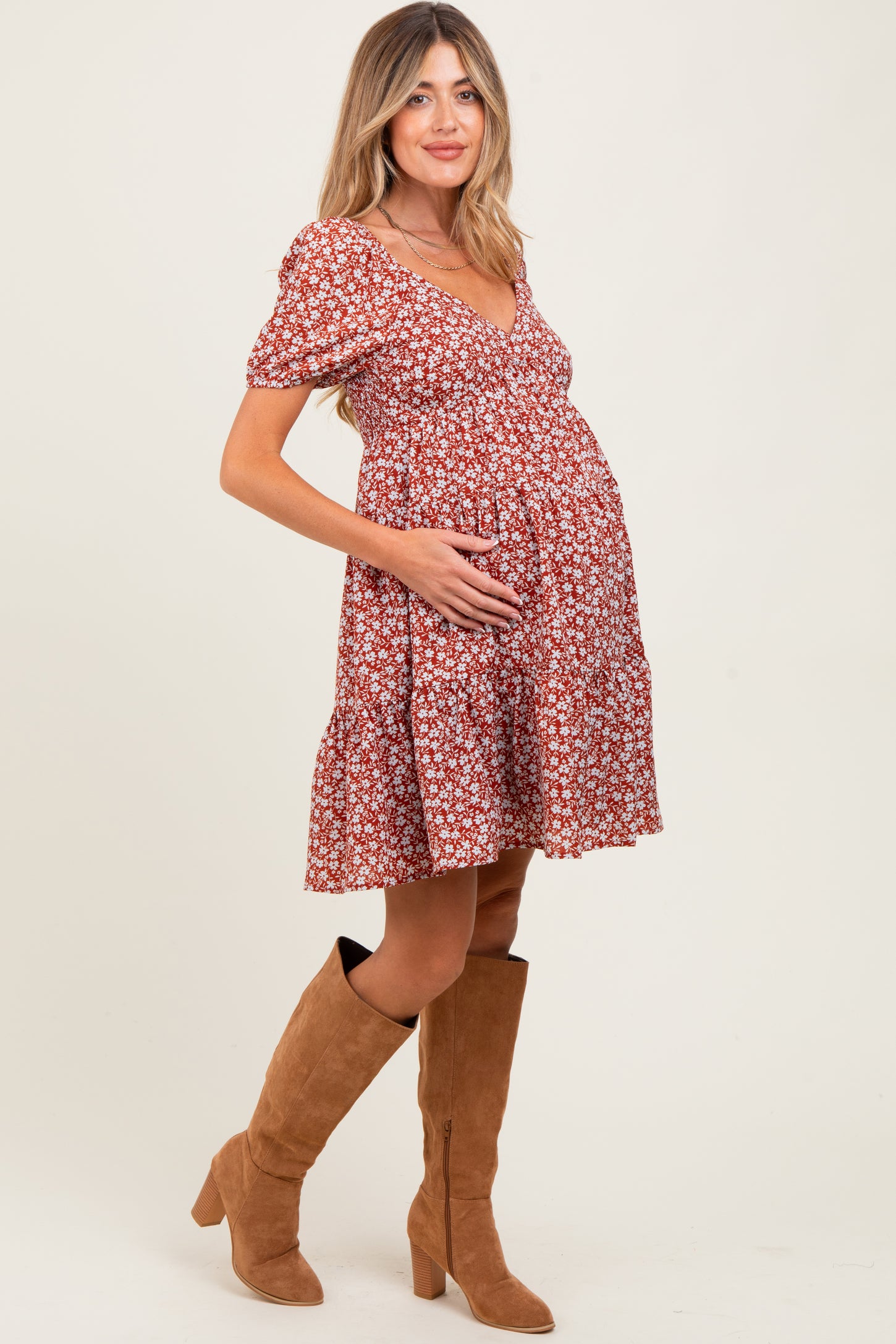 woman wearing a rust floral maternity dress with short puff sleeves and a tiered skirt, holding her baby bump