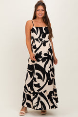 woman wearing a black and white floral print maternity maxi dress with adjustable straps and a ruffled hem, showing baby bump
