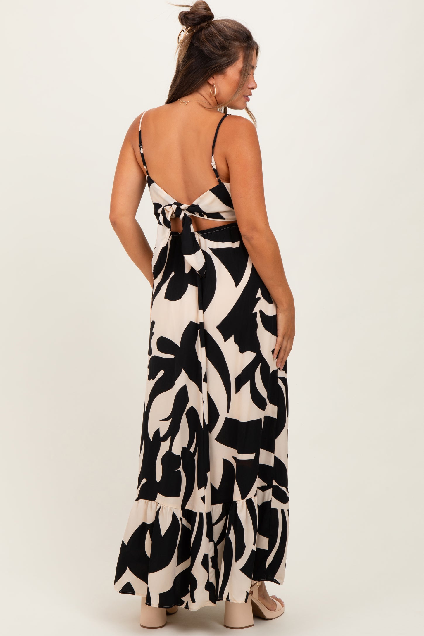 woman wearing a black and cream patterned maternity maxi dress with a back tie detail and a tiered hem
