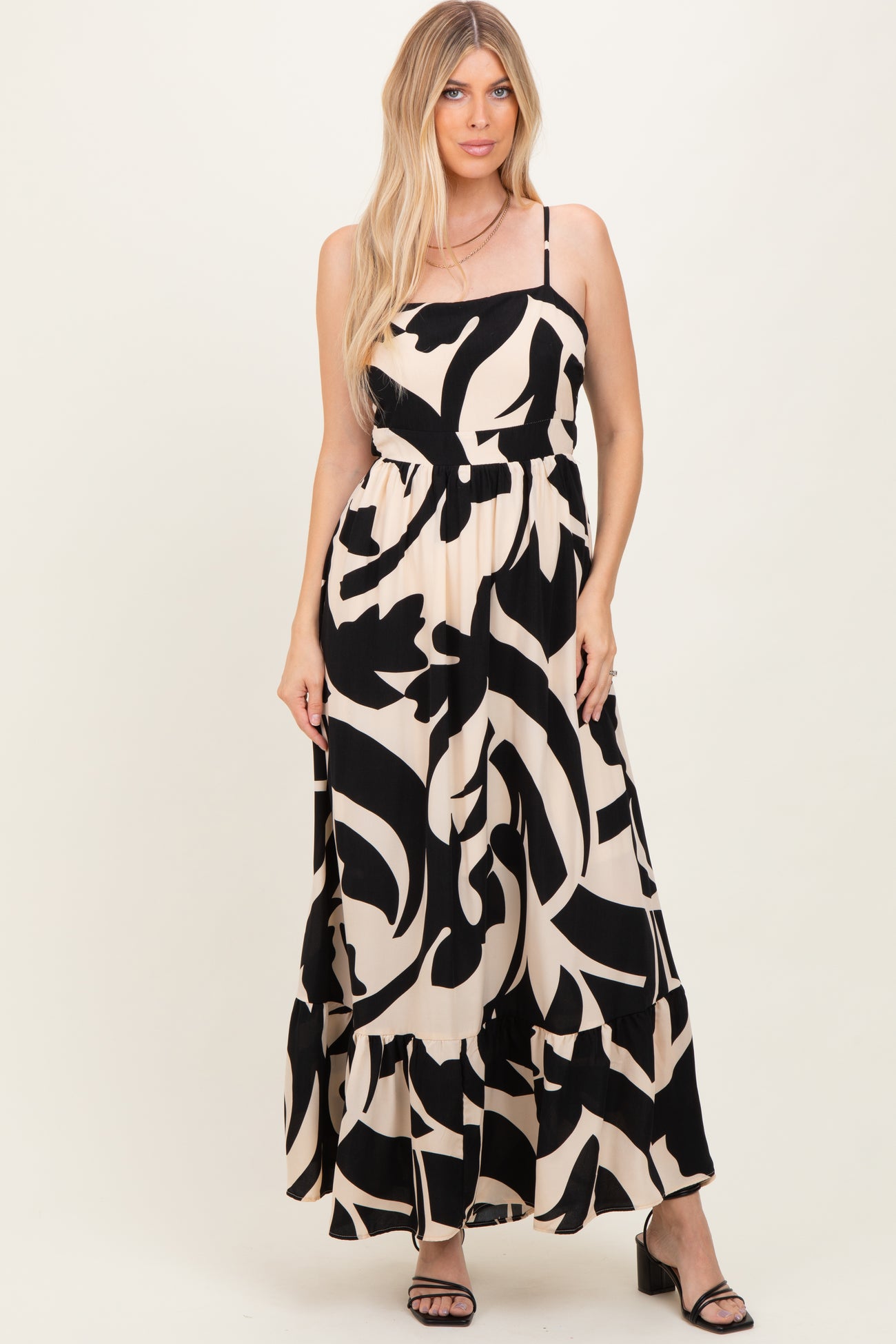 woman wearing a black and cream maxi dress with abstract print and tiered hem, standing and smiling