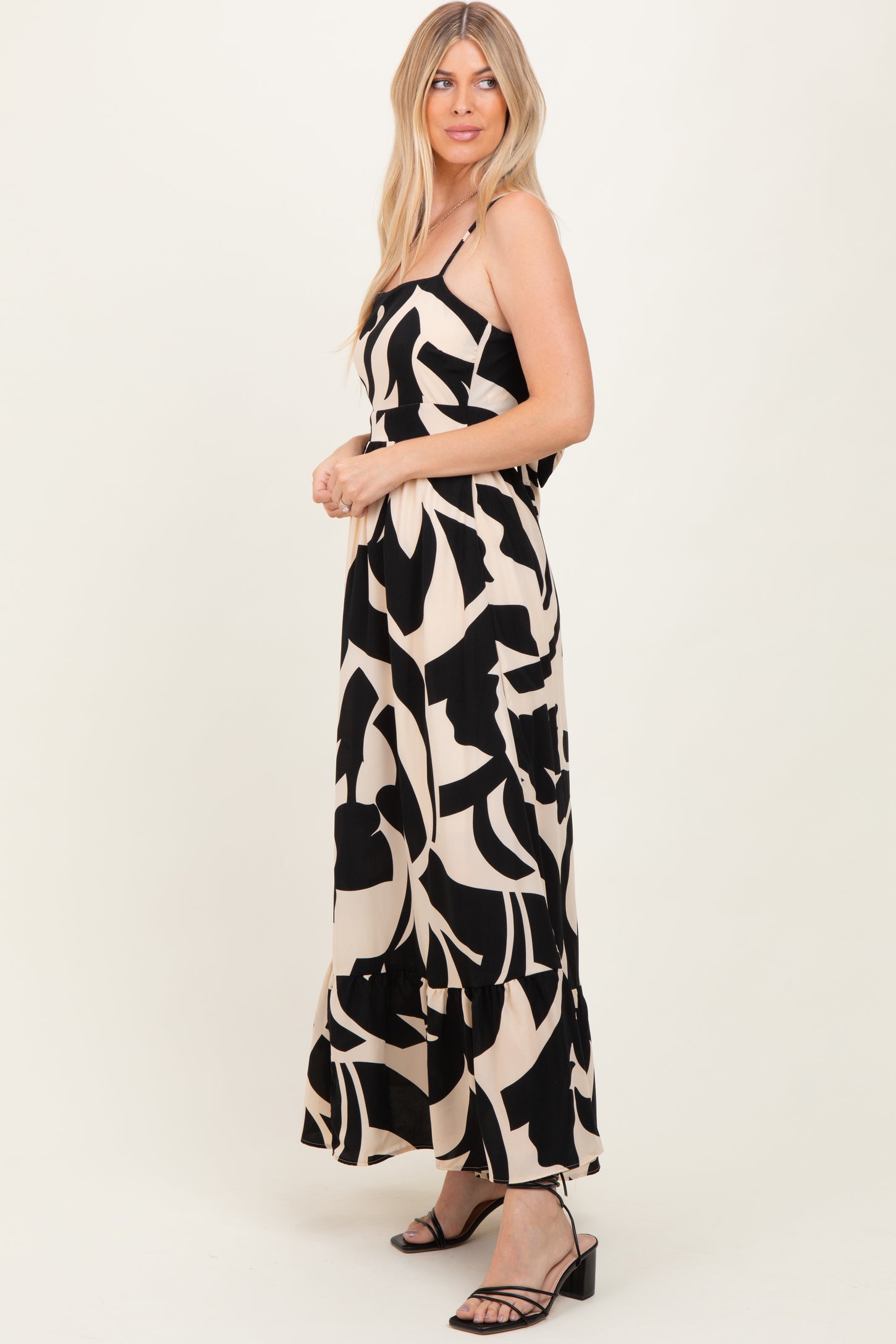 woman wearing a black and beige floral print maxi dress with spaghetti straps and a ruffled hem