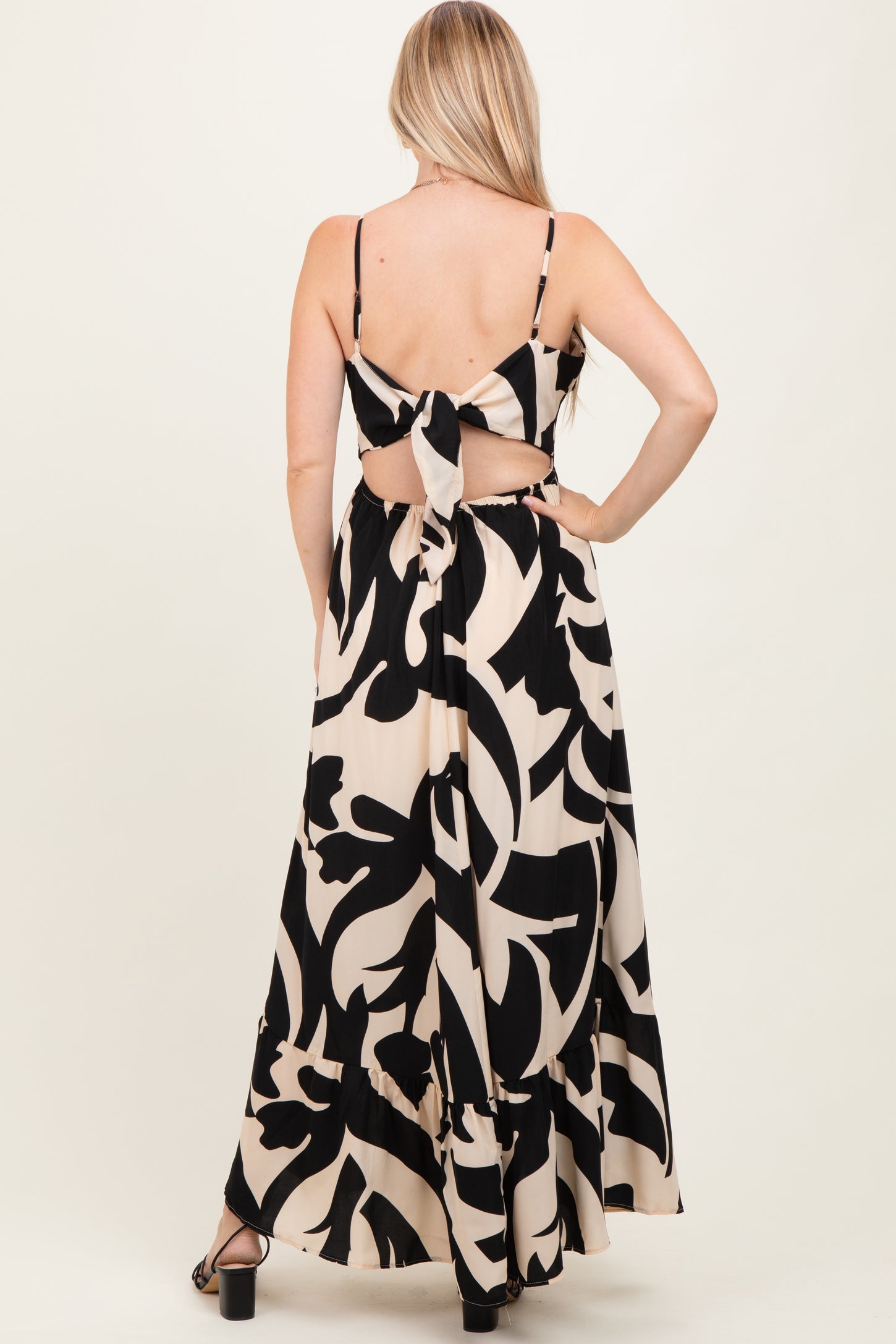 woman wearing a black and beige floral print maxi dress with a tied back detail and adjustable straps