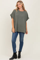woman wearing a loose-fitting olive green striped top with short sleeves paired with blue skinny jeans and black ankle boots
