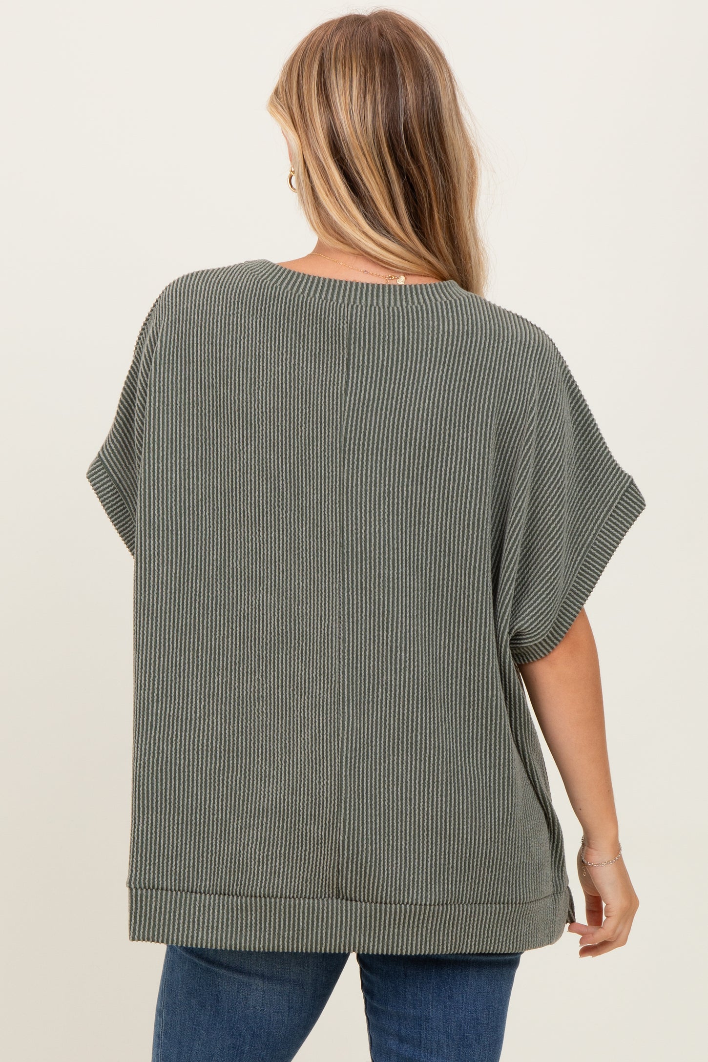 woman wearing a loose-fitting green ribbed top with short sleeves and a rounded hem, seen from the back