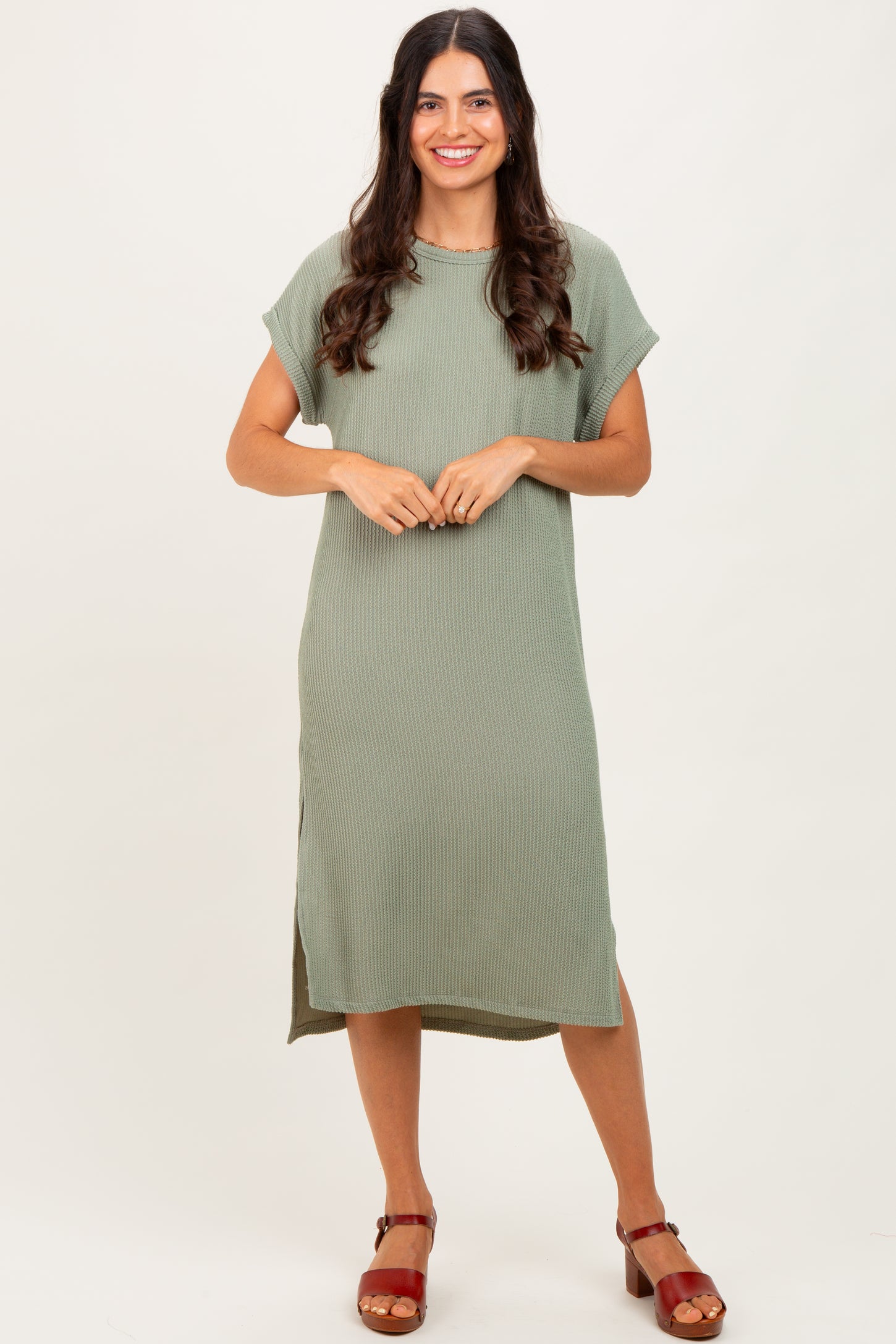 woman wearing a sage green ribbed midi dress with short sleeves and side slits, standing on a neutral background