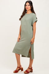 woman wearing a green ribbed midi dress with short sleeves and a side slit, paired with brown block-heel sandals