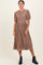 woman wearing a brown checked midi dress with smocked bodice and short puff sleeves, paired with black ankle boots