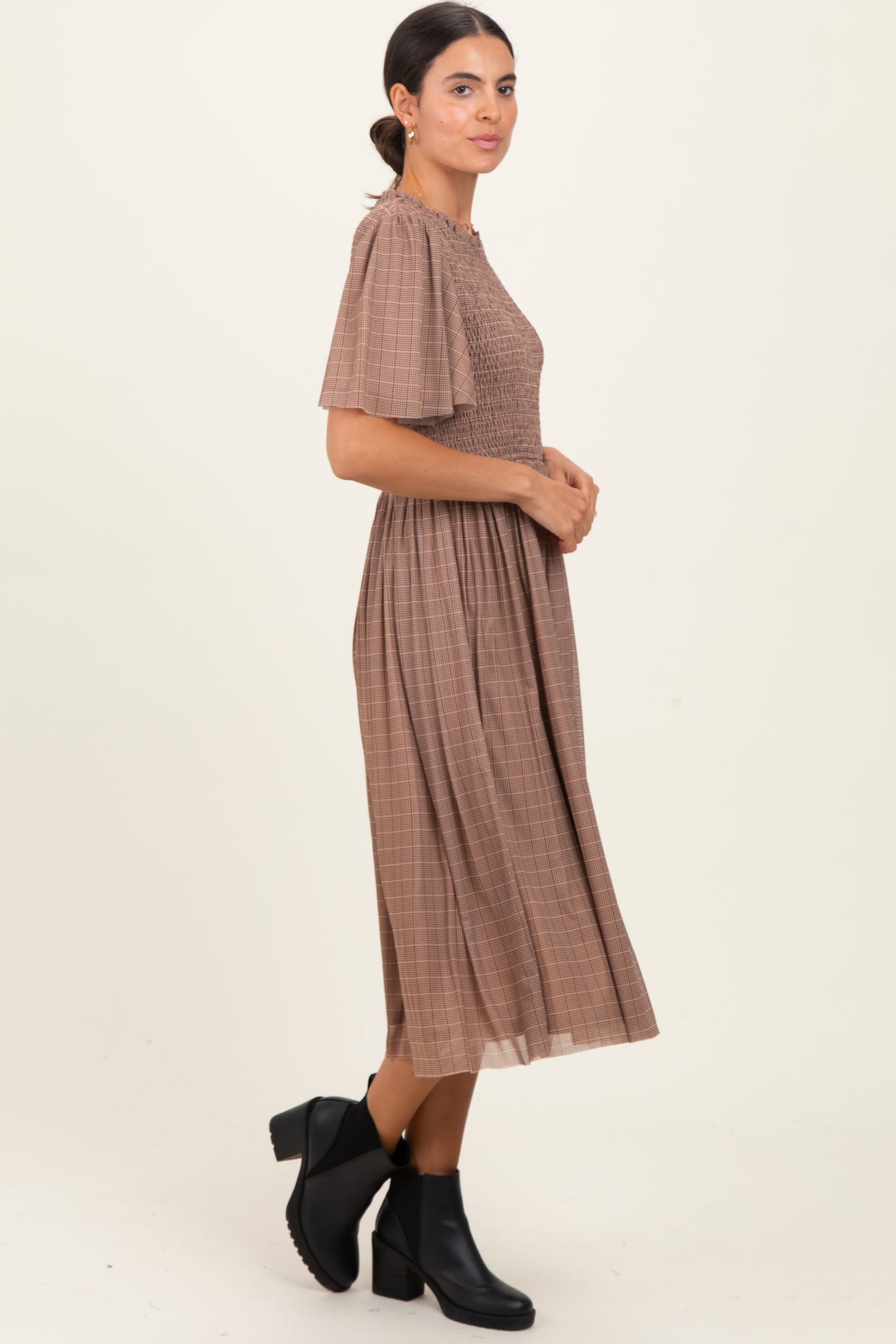 woman wearing a brown plaid midi dress with short sleeves and a smocked bodice, paired with black ankle boots