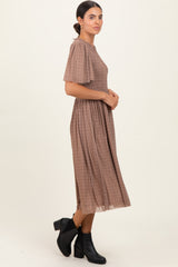 woman wearing a brown plaid midi dress with short sleeves and a smocked bodice, paired with black ankle boots