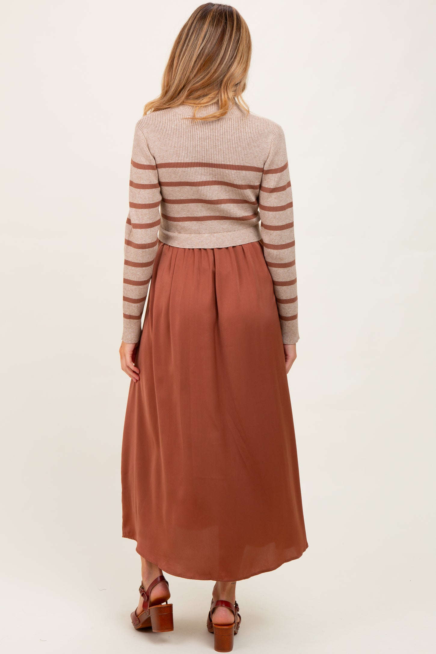 woman wearing a striped long sleeve maternity sweater and a flowy maxi skirt in rust color, with baby bump visible