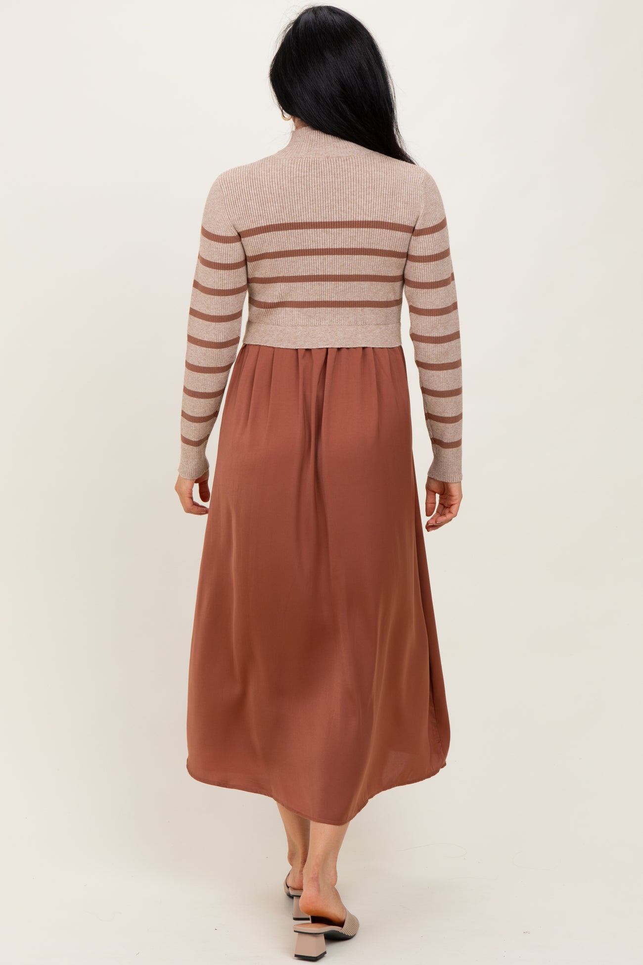 woman wearing a beige striped long sleeve sweater top with a rust colored maxi dress, viewed from the back