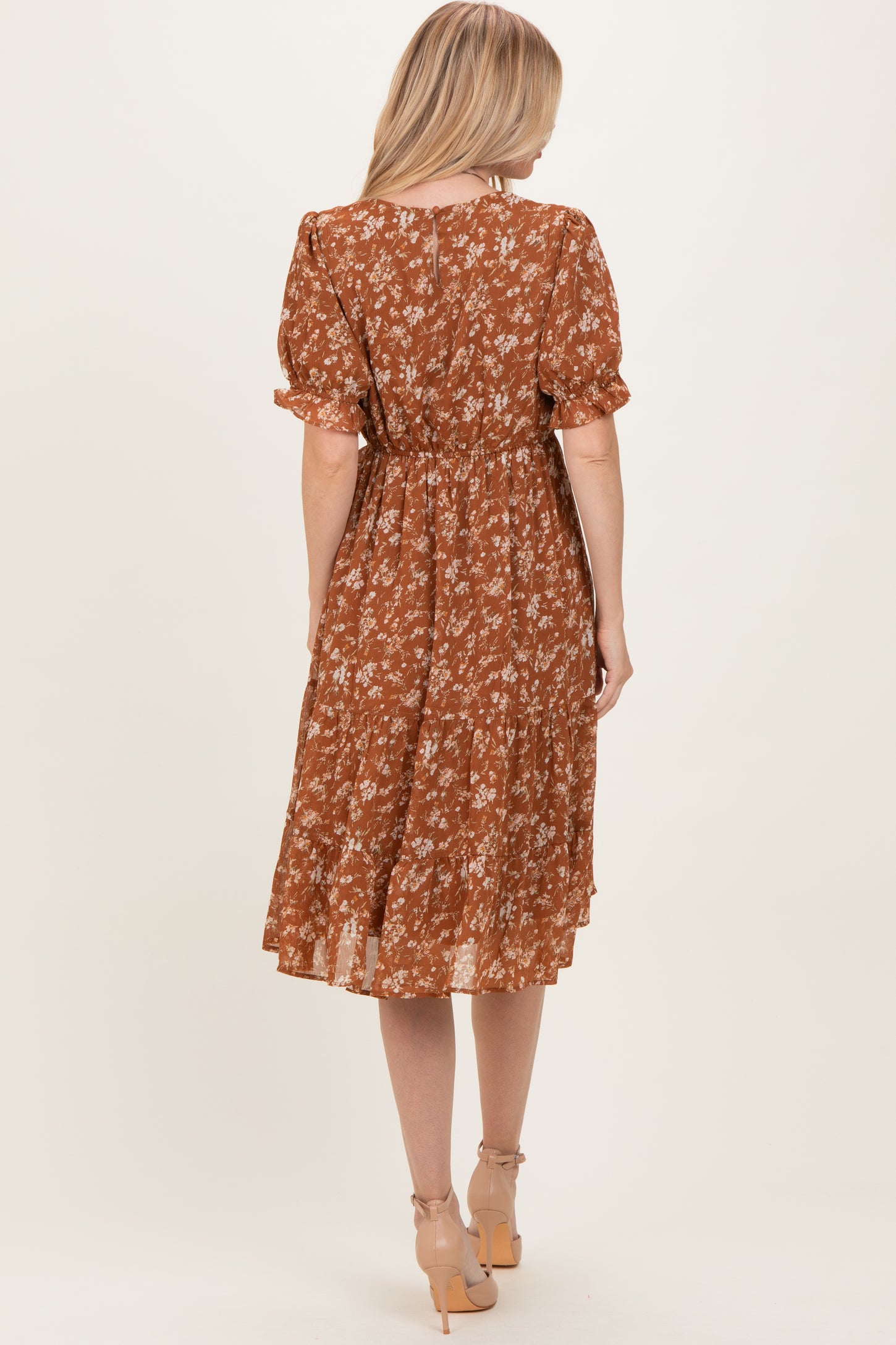 woman wearing a brown floral midi dress with short puff sleeves and a cinched waist, standing with her back to the camera