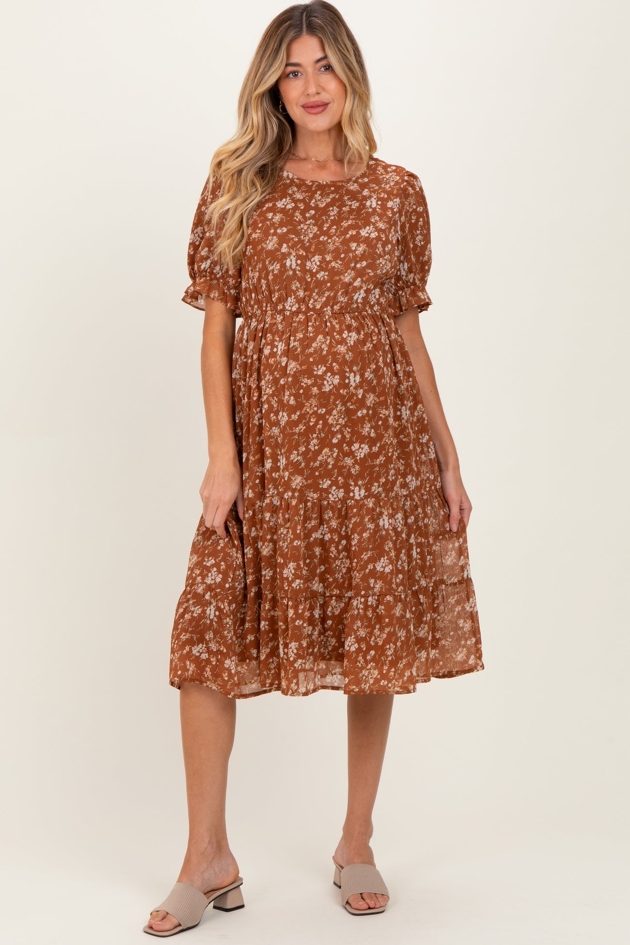 woman wearing a brown floral print maternity dress with short sleeves and a flowing skirt, showing a baby bump
