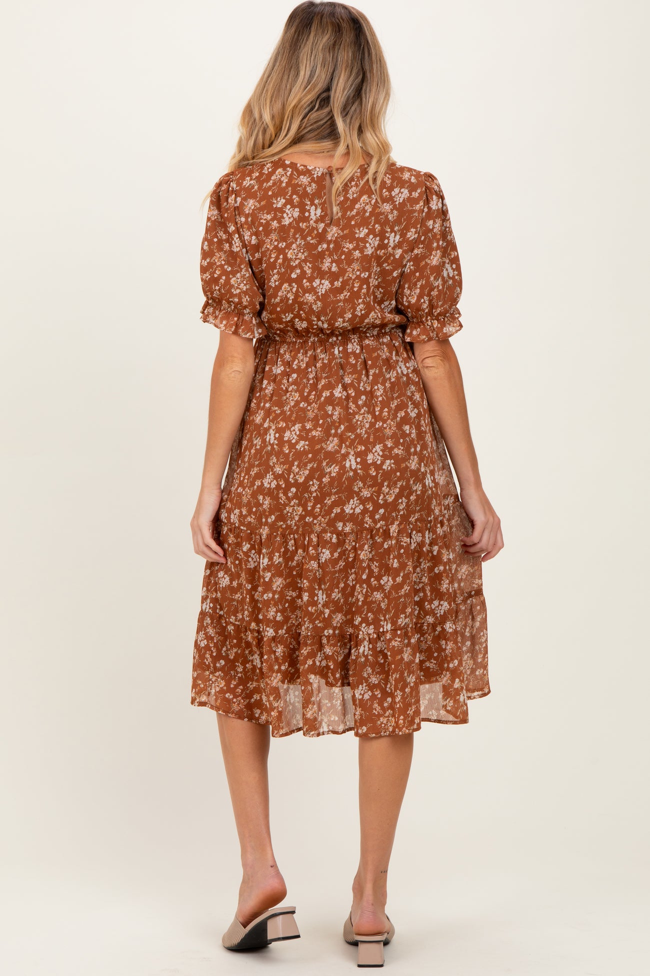 woman wearing a brown floral maternity dress with ruffle sleeves and a tiered skirt, showing her back