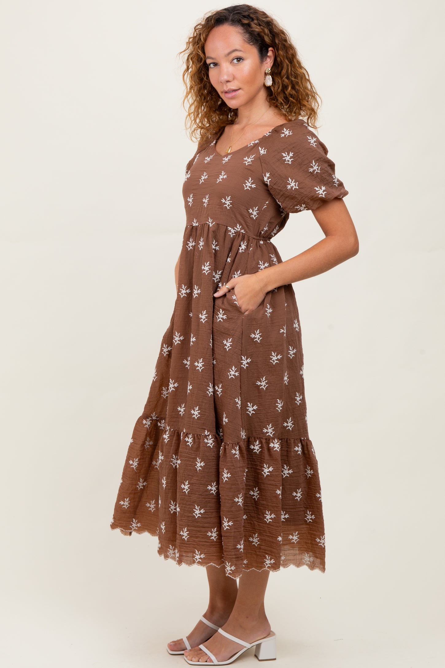 woman wearing a brown floral maxi dress with puff sleeves and pockets, standing sideways against a neutral background