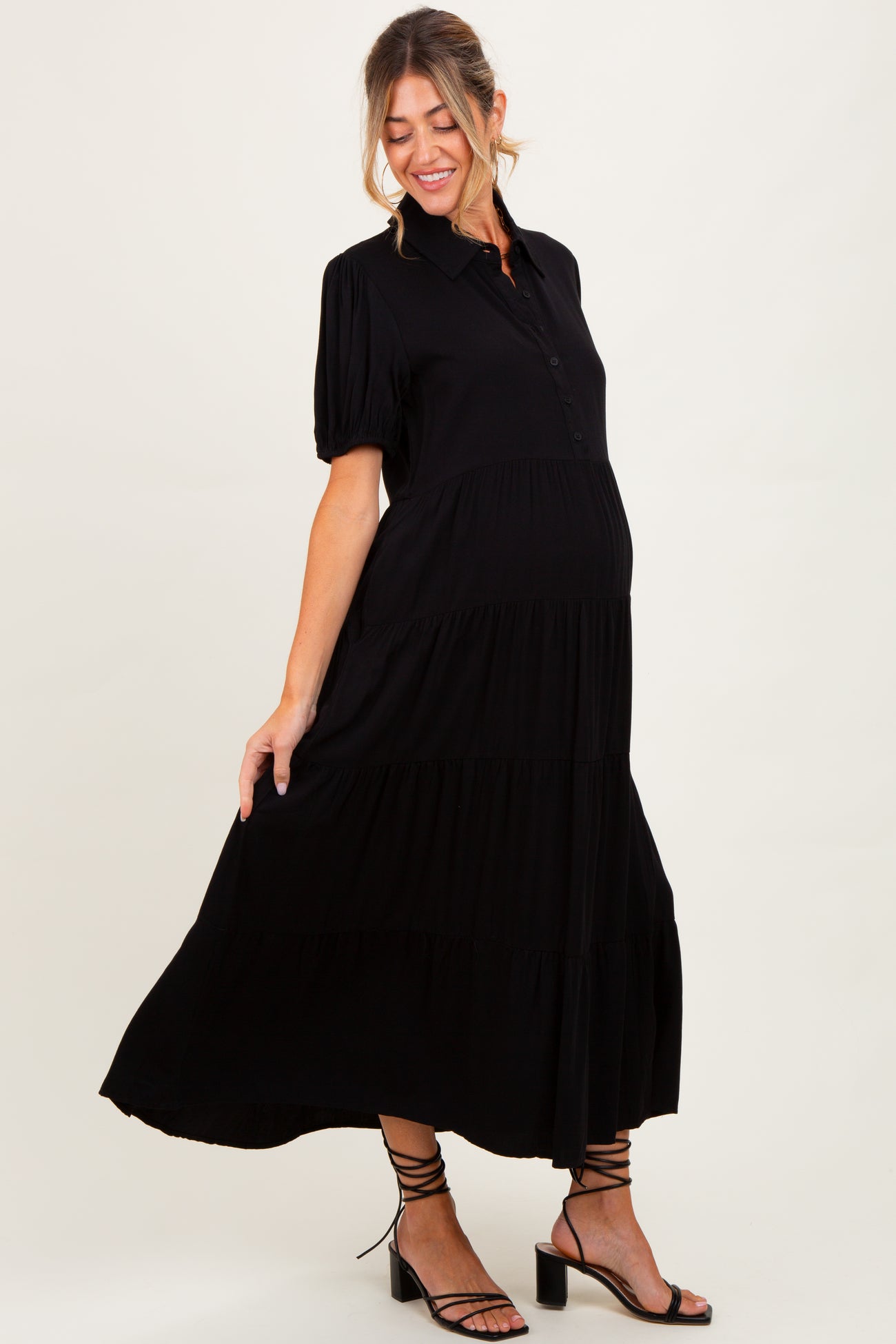 woman wearing a black maternity maxi dress with puff sleeves and a tiered skirt, showcasing her baby bump