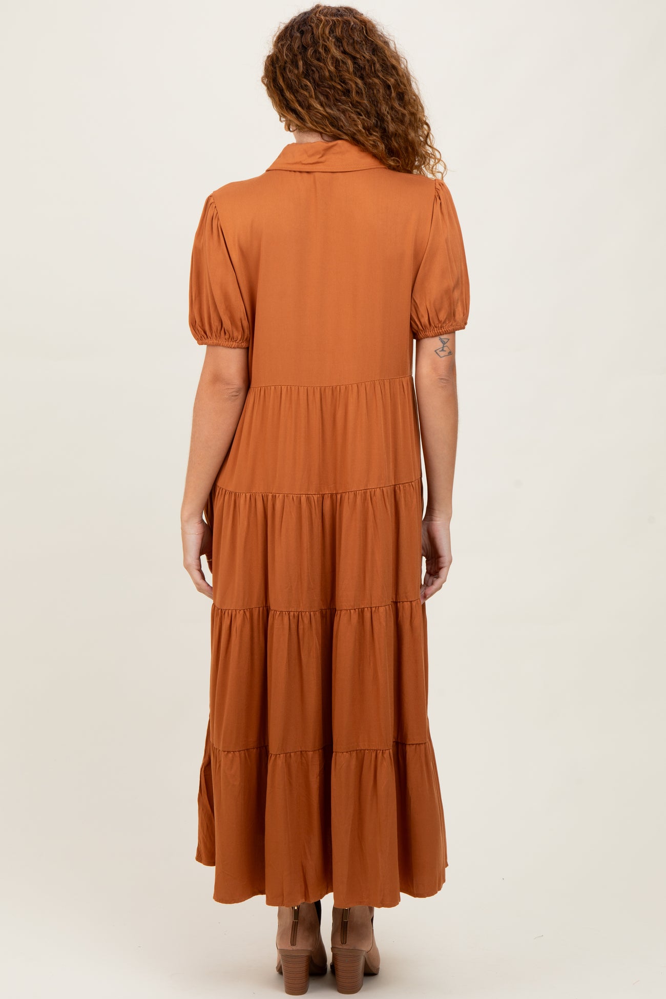 woman wearing a rust colored tiered maxi dress with puff sleeves and a collar, seen from the back