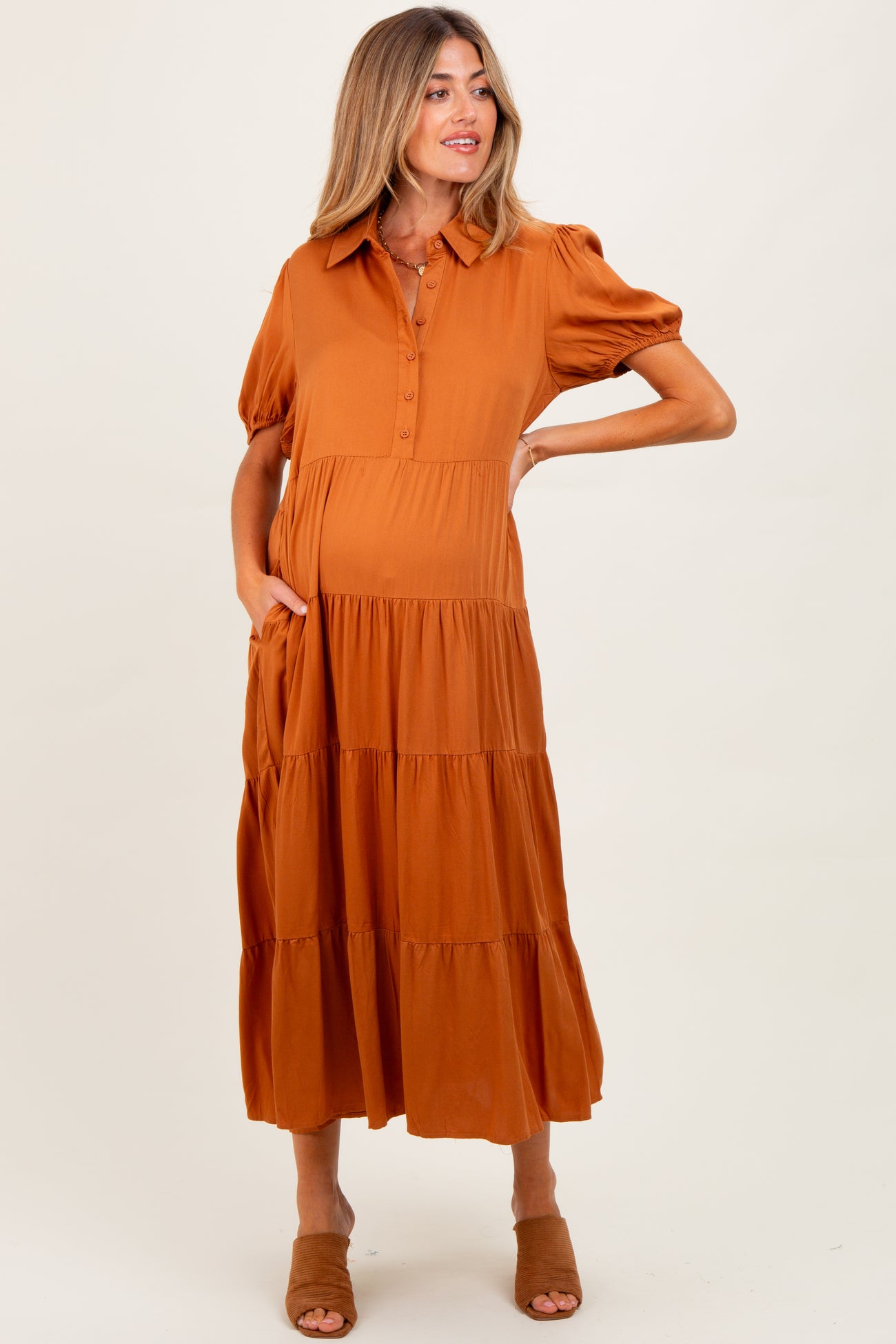 woman wearing an orange button-up maternity dress with short puff sleeves and a tiered skirt, holding her baby bump
