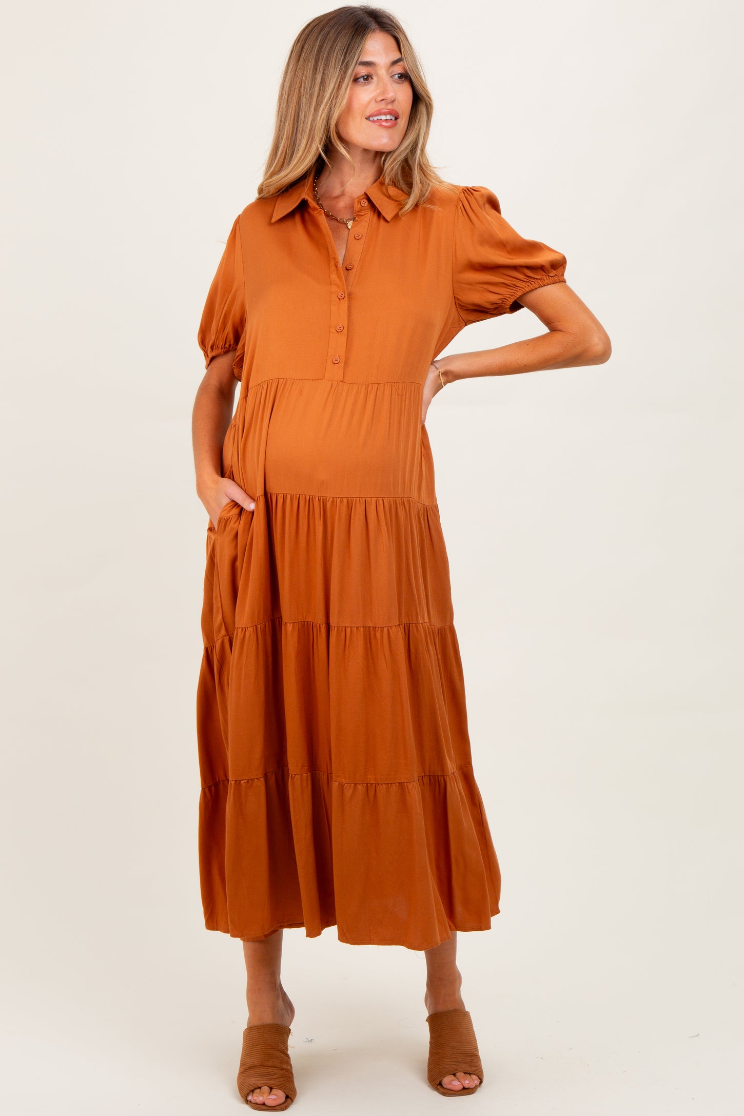 woman wearing an orange button-up maternity dress with short puff sleeves and a tiered skirt, holding her baby bump