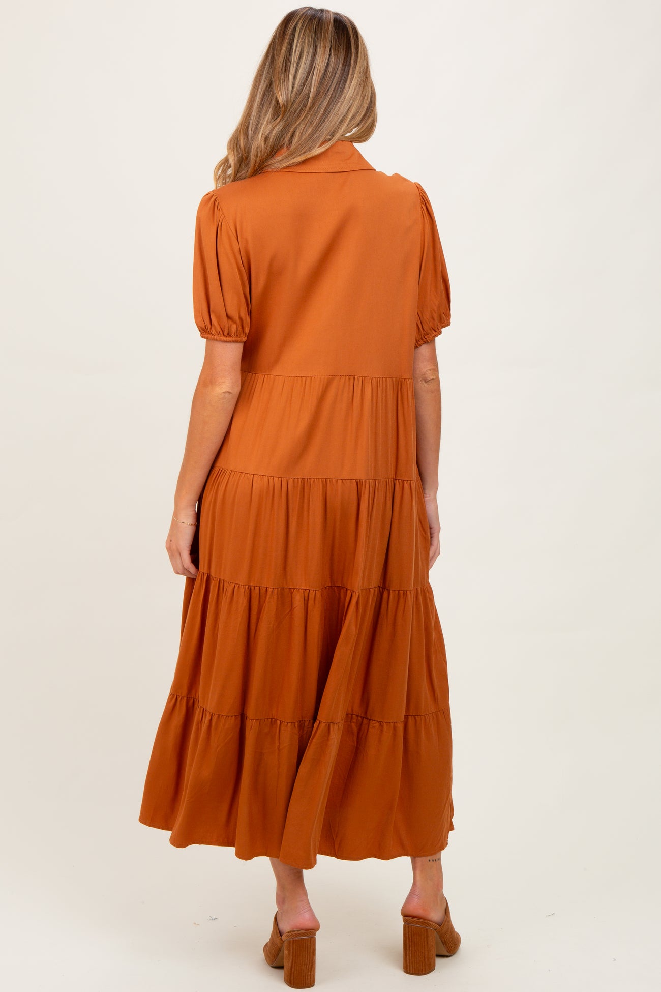 woman wearing a rust-colored maternity tiered maxi dress with short puff sleeves and a buttoned collar