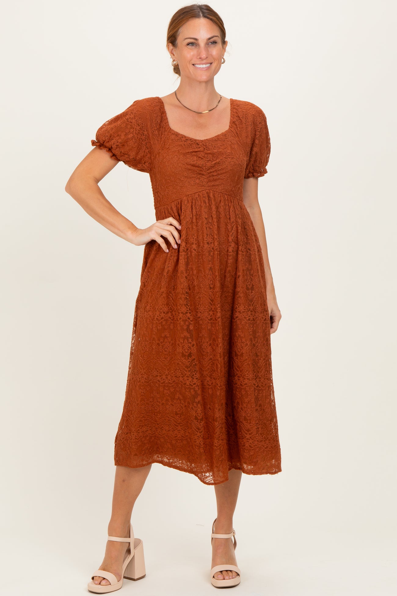 woman wearing a rust-colored lace midi dress with puff sleeves and a square neckline in a standing pose