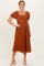 woman wearing a rust-colored lace midi dress with puff sleeves and a square neckline in a standing pose
