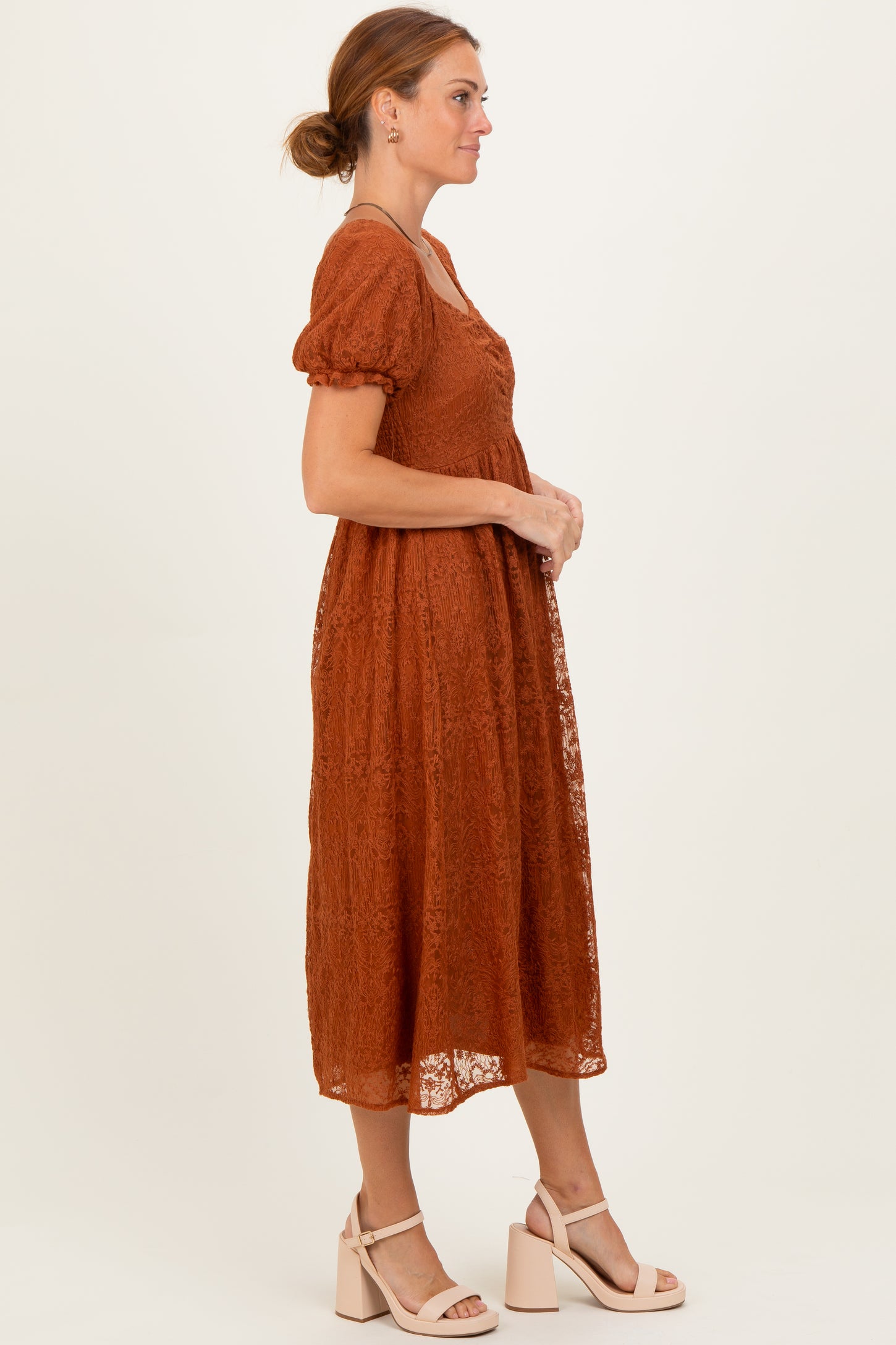 woman wearing an rust-colored lace midi dress with puff sleeves and a cinched waist, standing in profile