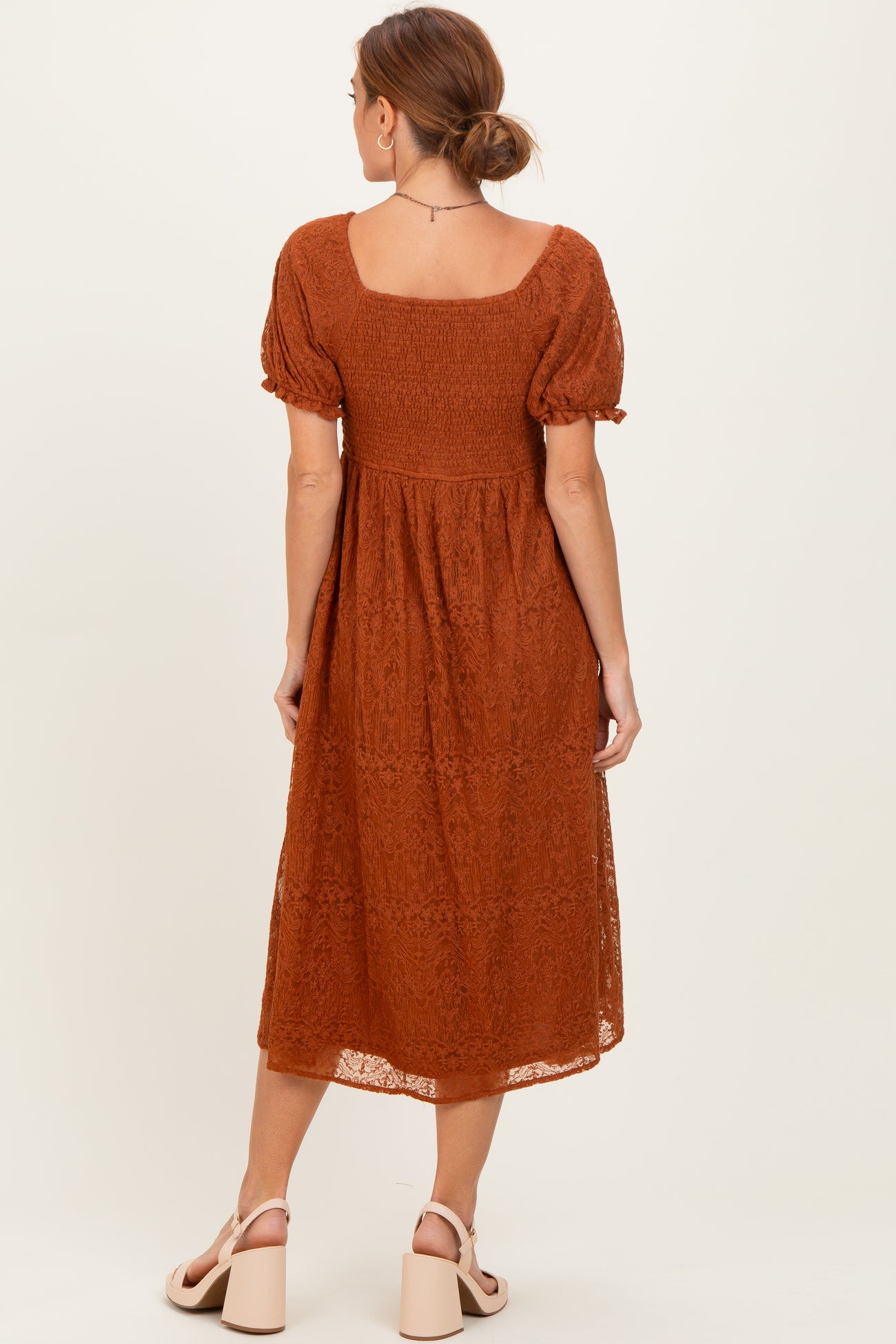woman wearing a rust-colored lace midi dress with short puff sleeves and a smocked bodice, showing the back view