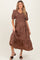 woman wearing a brown floral maternity dress with a v-neckline and puff sleeves, holding the skirt slightly