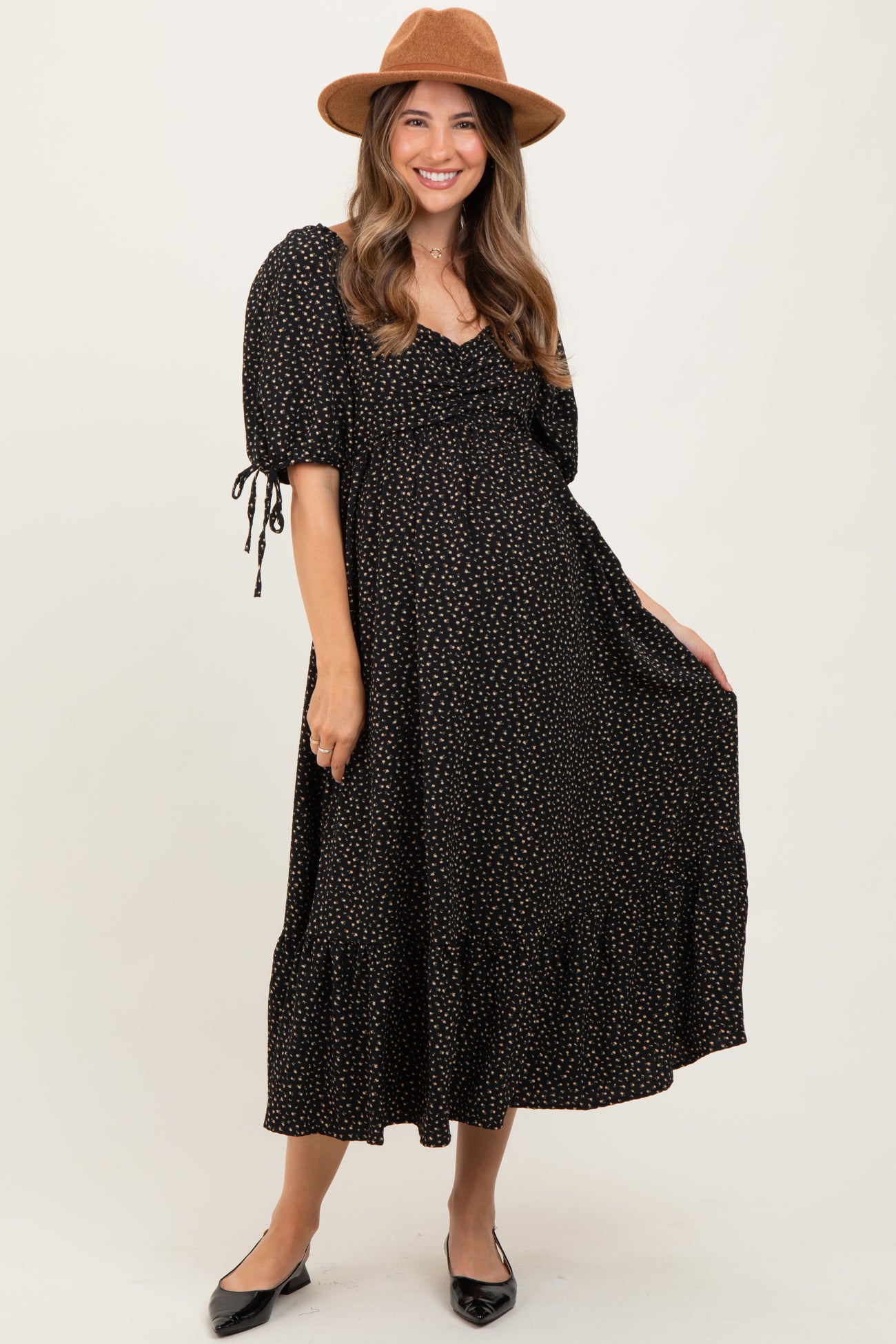 woman wearing a black maternity dress with white polka dots and puff sleeves, smiling and holding her baby bump