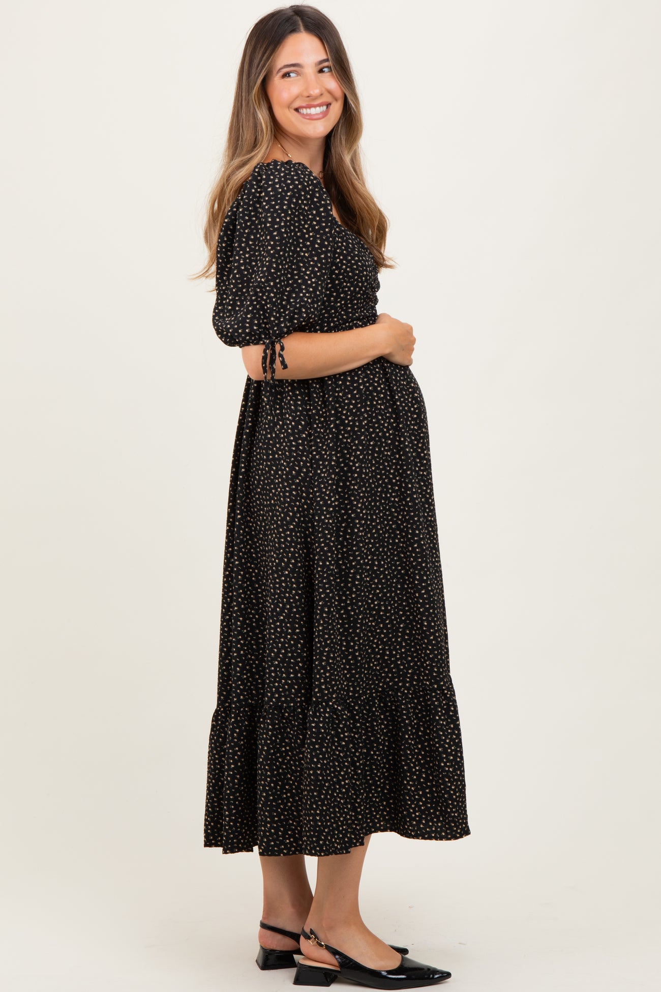 woman wearing a black maternity dress with puff sleeves and a tiered skirt, holding her baby bump