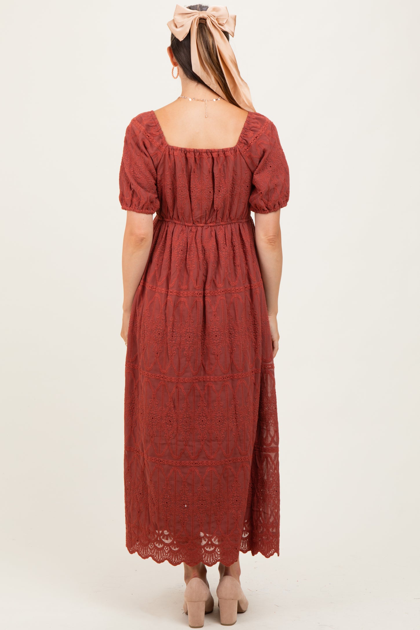 woman wearing a rust red lace maternity dress with puff sleeves and a mid-calf length skirt, seen from the back