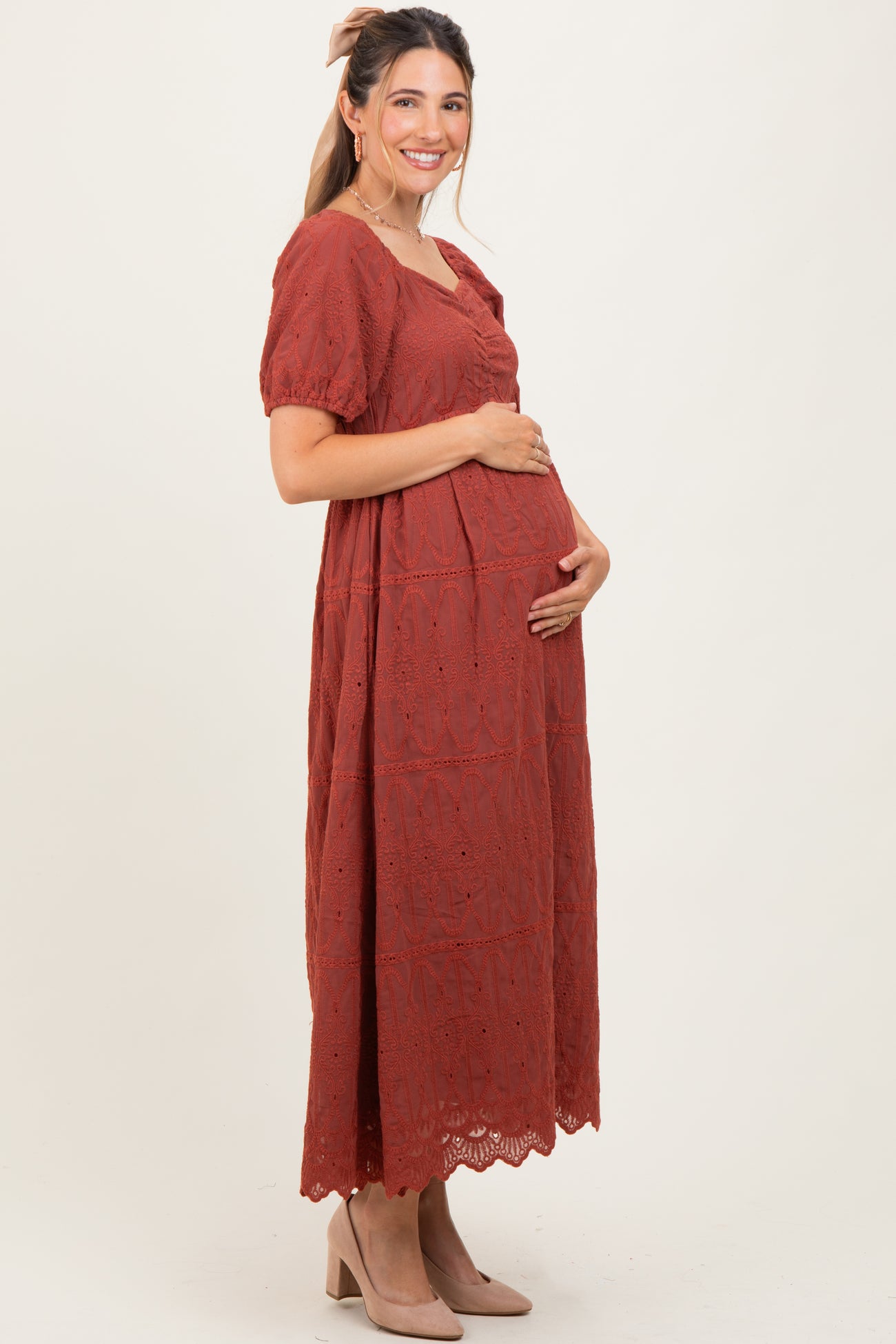 woman wearing a rust long sleeve maternity dress with lace details and holding her baby bump.