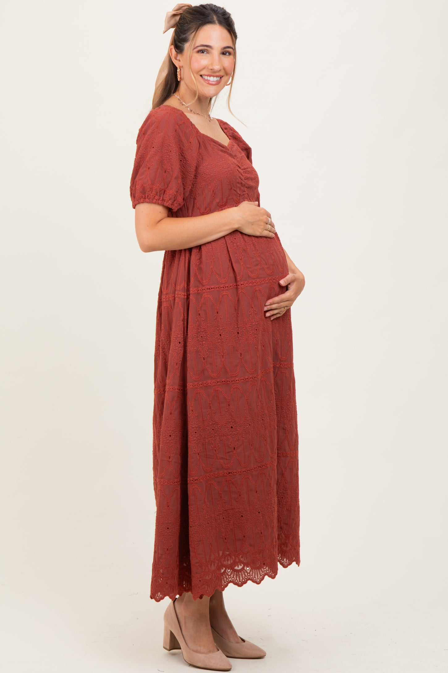 woman wearing a rust long sleeve maternity dress with lace details and holding her baby bump.
