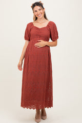 woman wearing a rust-colored maternity maxi dress with puff sleeves and a cinched bodice, showcasing her baby bump