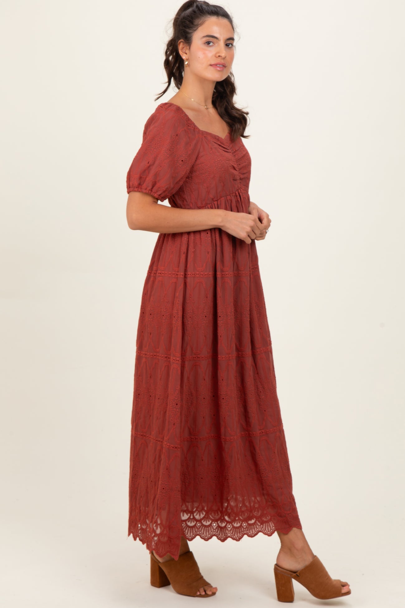 woman wearing a rust-colored puff sleeve maxi dress with embroidered details and a tiered skirt, paired with brown heeled sandals