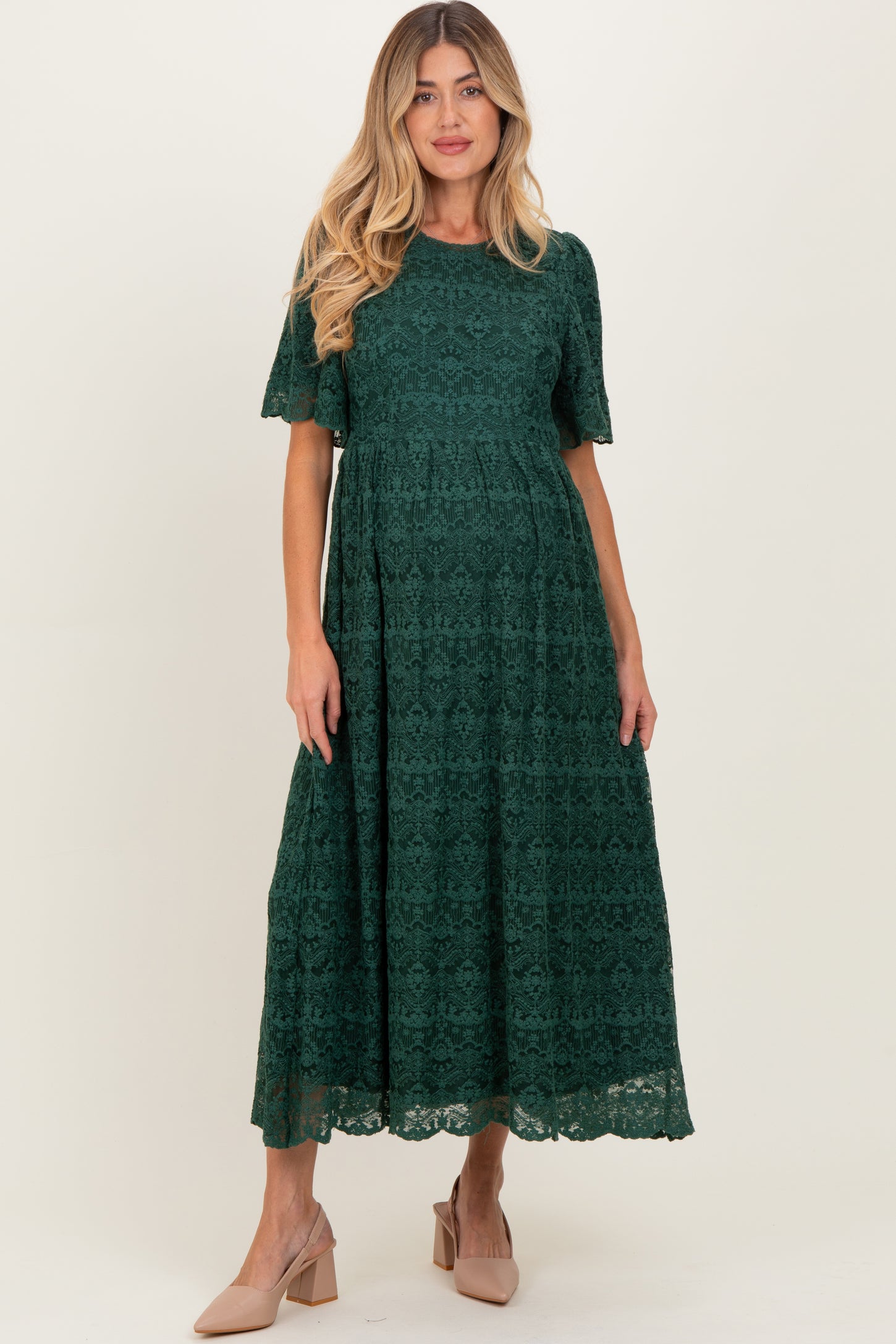 woman wearing a dark green lace short sleeve maternity dress with a flowing skirt and a fitted bodice