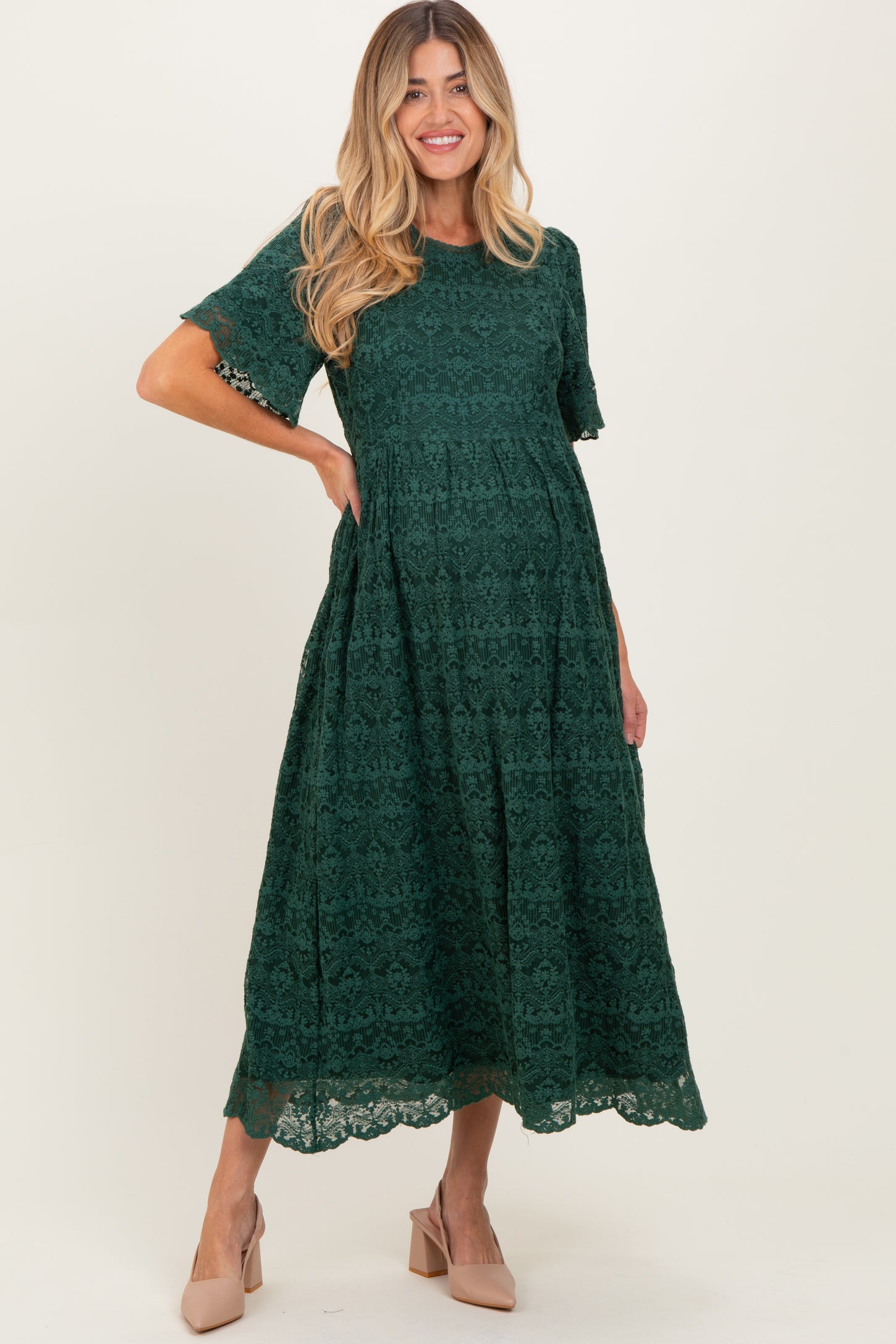 woman wearing a dark green lace maternity dress with short sleeves and a tiered skirt, showcasing her baby bump