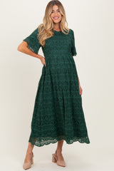 woman wearing a dark green lace maternity dress with short sleeves and a tiered skirt, showcasing her baby bump