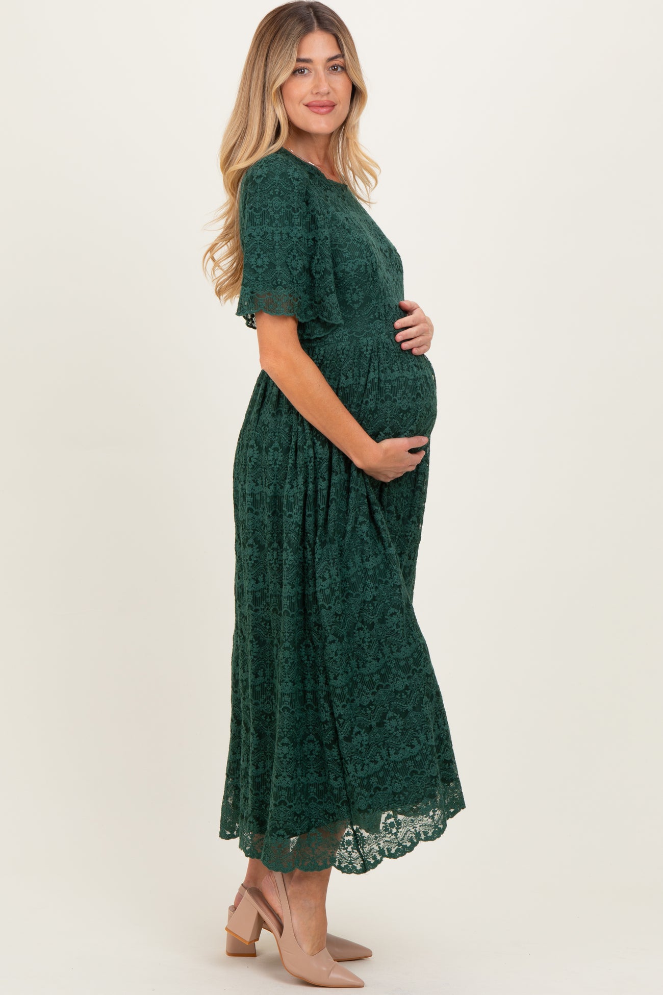 woman wearing a dark green lace maternity dress and holding her baby bump