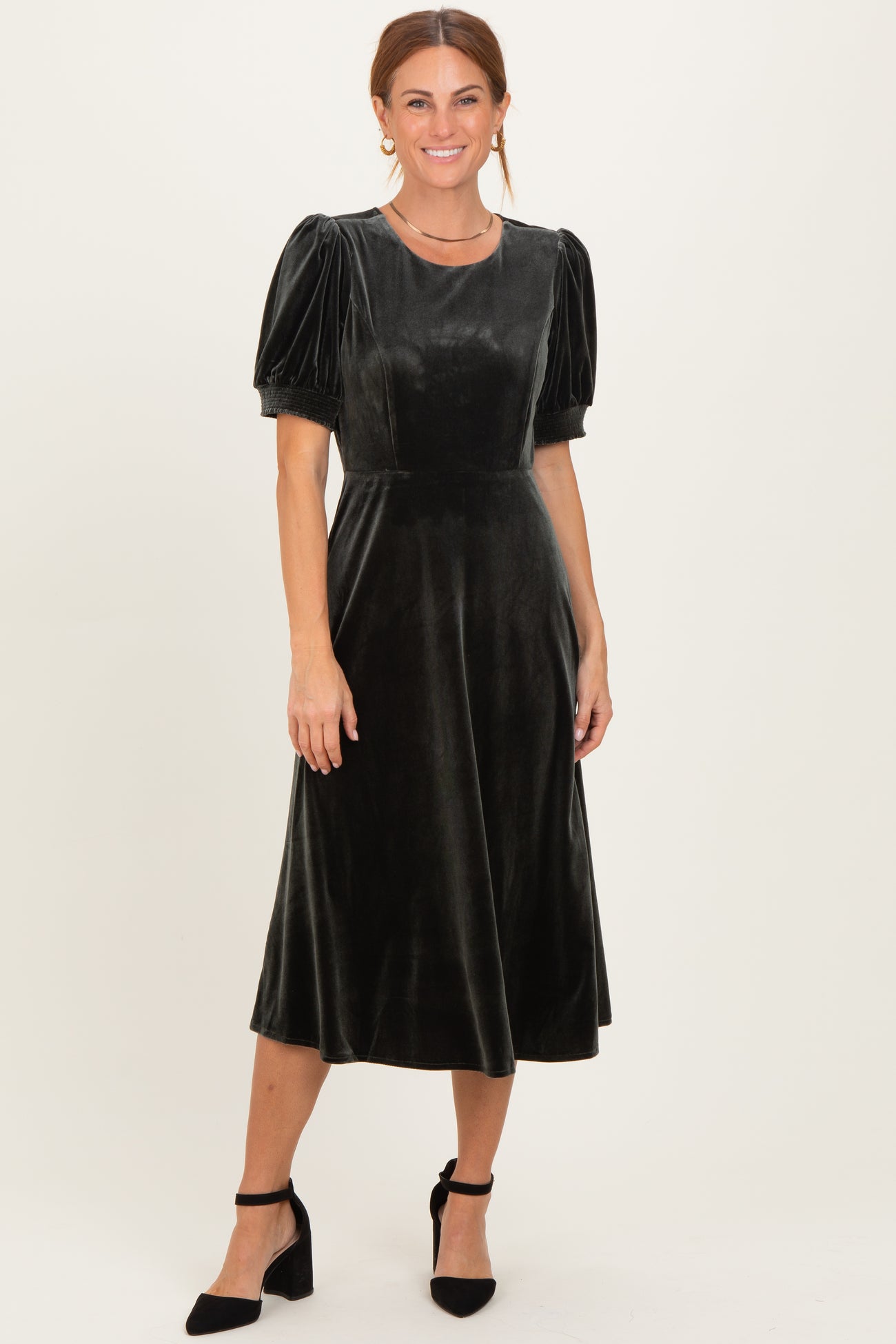 woman wearing a dark green velvet midi dress with puff sleeves and a fitted bodice, styled with black heels