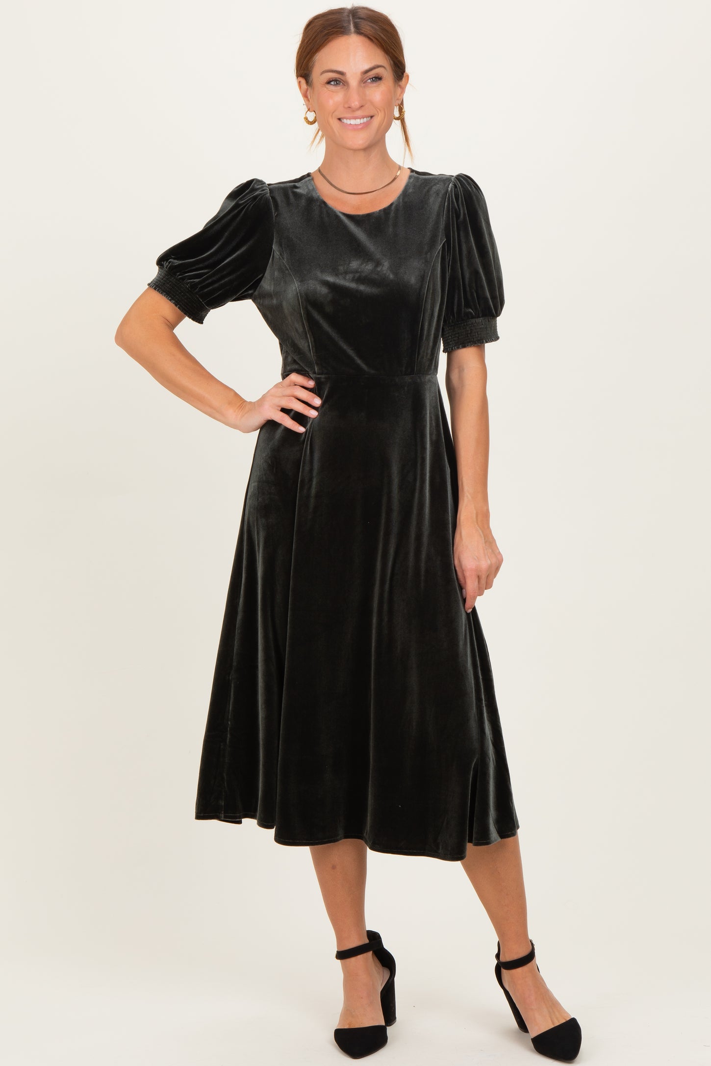 woman wearing a black velvet midi dress with puff sleeves and a fitted bodice, styled with black heels