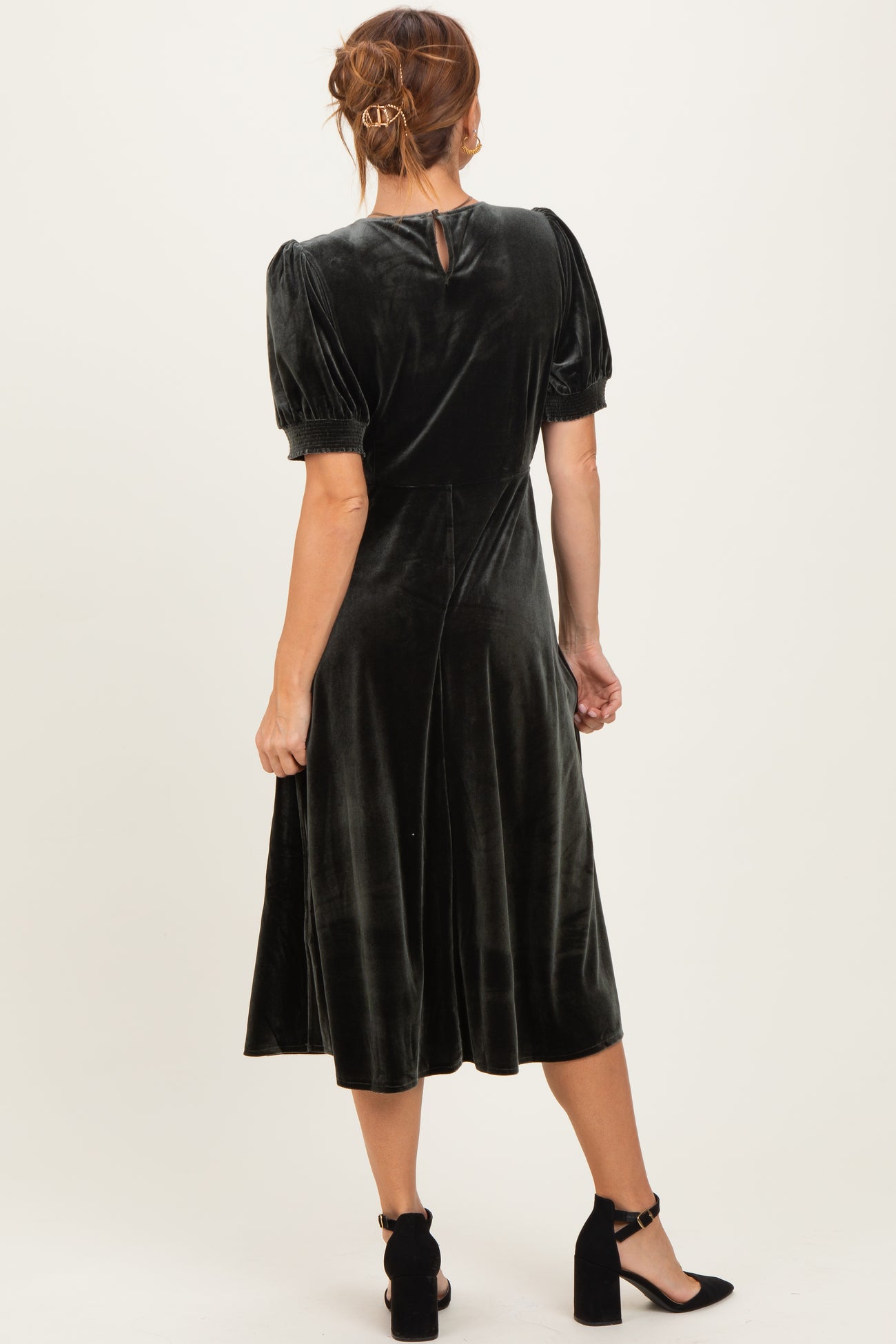woman wearing a green velvet midi dress with puff sleeves and a keyhole back, styled with black heels