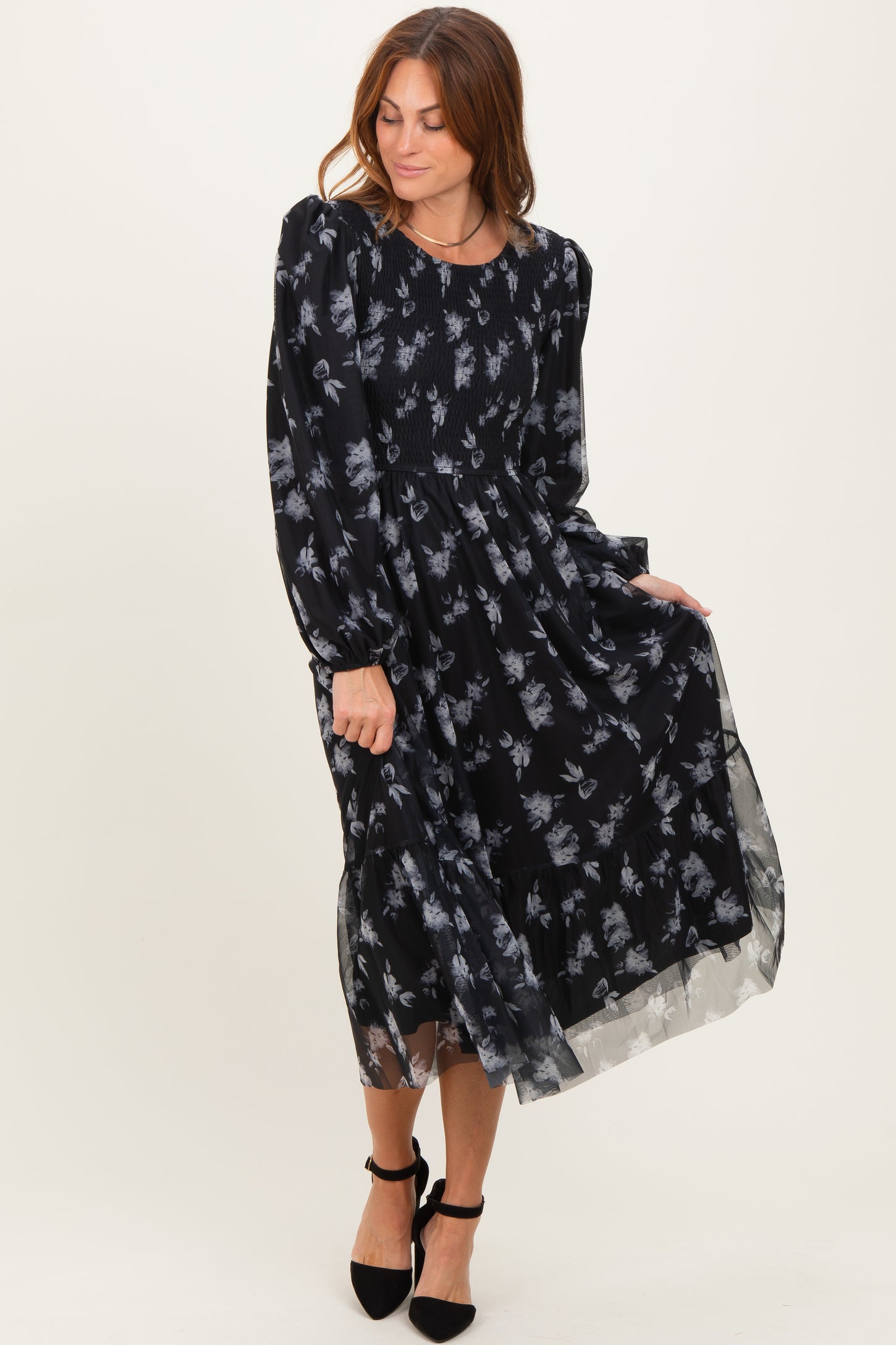 woman wearing a black floral long sleeve maxi dress with a smocked bodice and layered skirt, posing elegantly