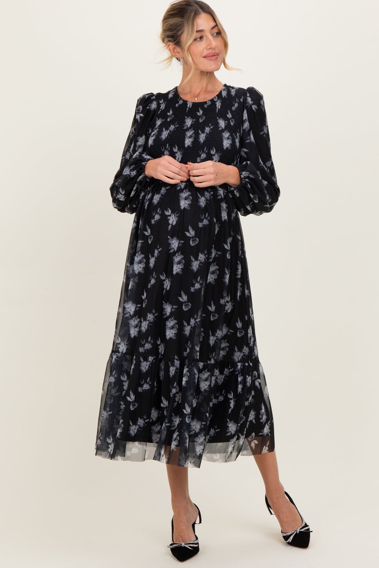 woman wearing a black floral maternity dress with long puff sleeves and a gathered waist, showcasing her baby bump