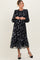 woman wearing a black floral maternity dress with long puff sleeves and a gathered waist, showcasing her baby bump