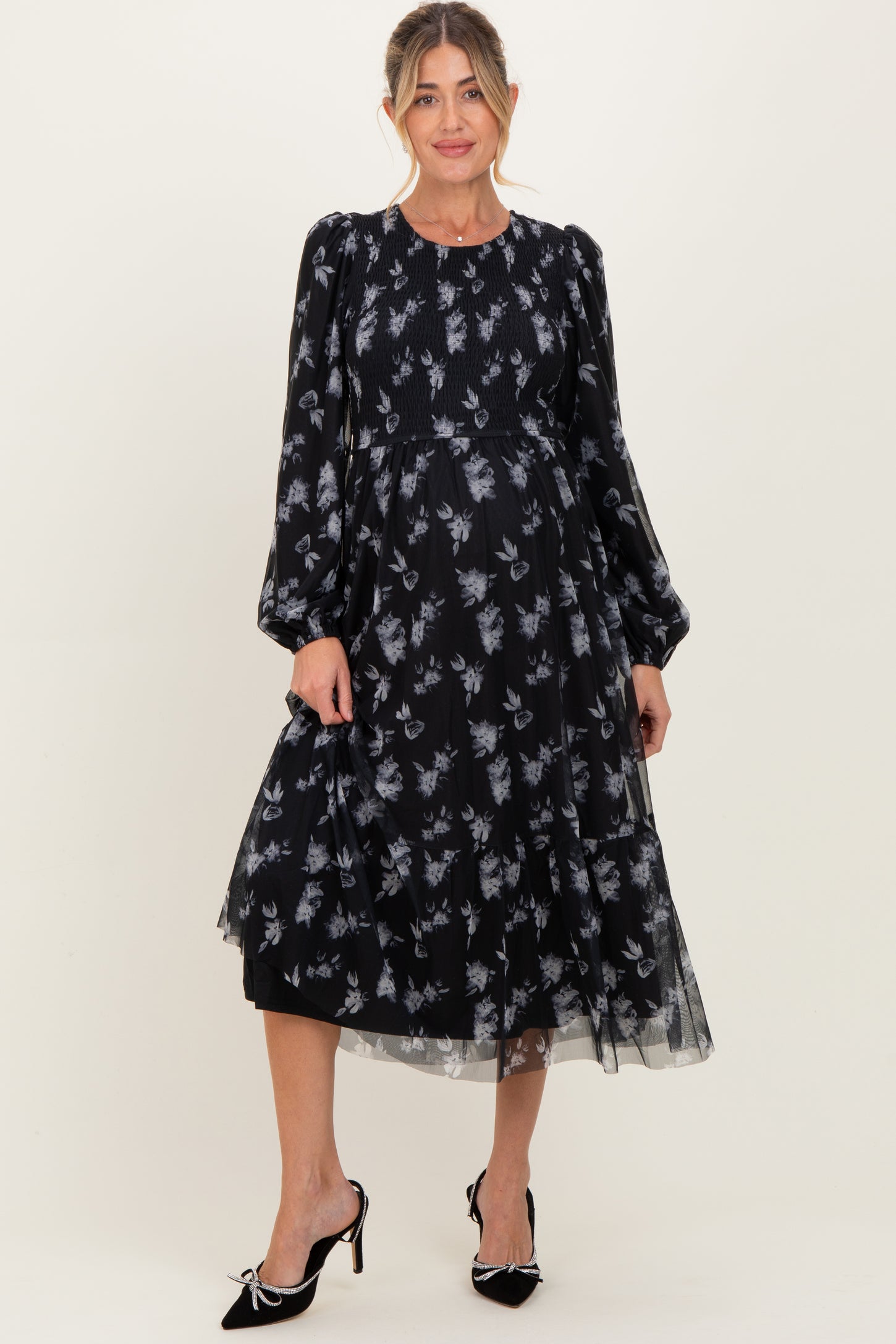woman wearing a black floral print maternity dress with puff sleeves and a flowy skirt, showcasing a baby bump