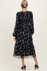 woman wearing a black maternity dress with floral print and sheer ruffled hem, showing the back view